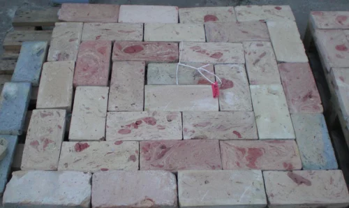 Stack of light red and beige bricks laid in a spiral pattern on a pallet, with a pink tag tied to string in the center.