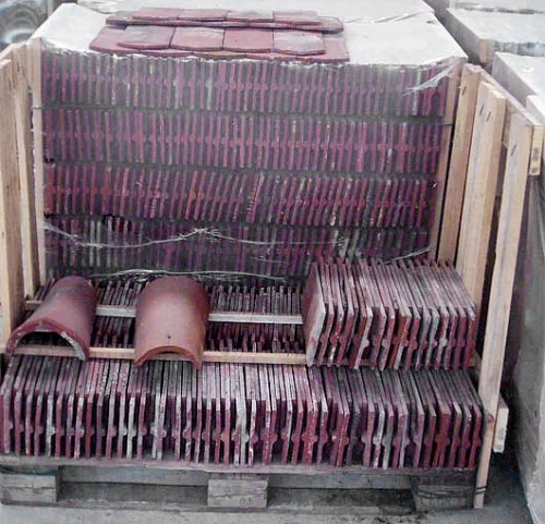 Stacked red clay roof tiles on a wooden pallet crate, showing curved and straight tile sections ready for installation