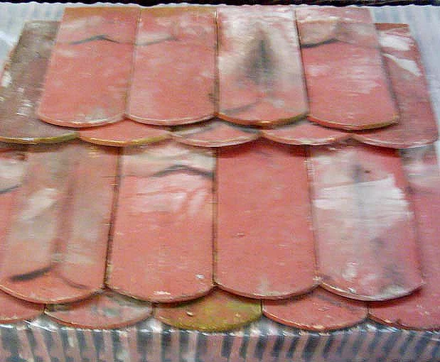 Close-up of red clay roof tiles overlapping in rows, with some white patches showing weathering.