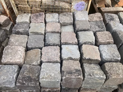 Stacks of square cobblestone pavers in gray and brown tones, arranged in neat rows for a paving project.