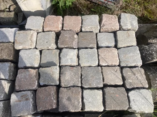 Stack of square cobblestone pavers arranged in a neat grid outdoors; stones range from gray to brown hues.