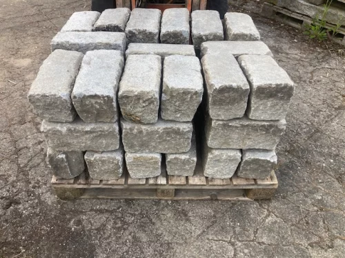 Stack of gray concrete blocks on a wooden pallet in an outdoor yard, ready for transport or storage.