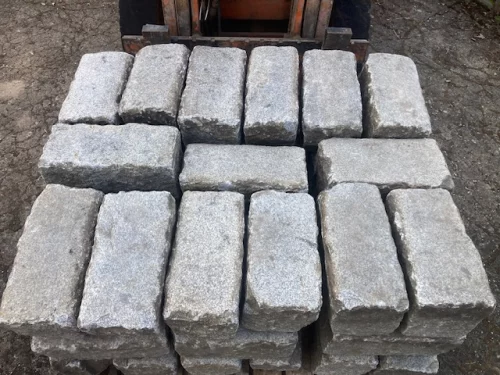 Stack of gray rectangular concrete pavers arranged in a compact pile on the ground (16 stones).