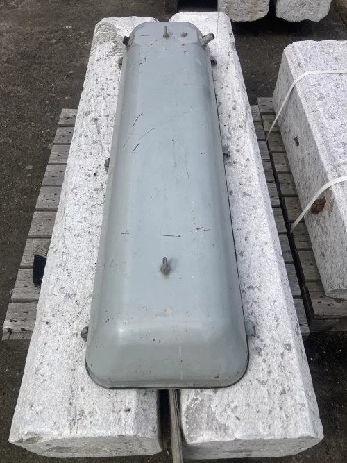 Grey metal cylindrical enclosure with bolts, resting on white stone blocks outdoors.