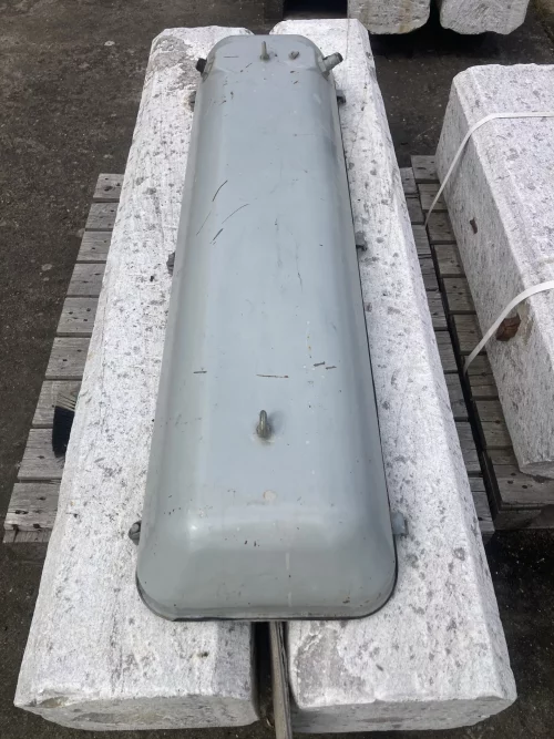 Grey metal cylindrical enclosure with bolts, resting on white stone blocks outdoors.