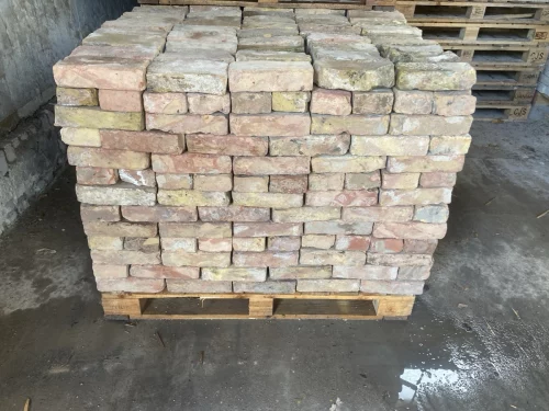 Stack of light-colored bricks neatly arranged on a wooden pallet in a storage area.